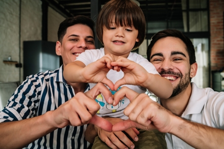 couple with adopted child making heart shapes with their hands